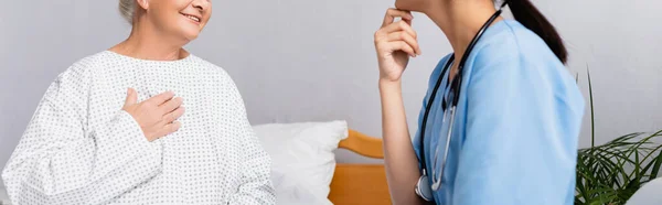 Abgeschnittene Ansicht einer lächelnden Seniorin, die die Brust berührt, während sie mit einer Krankenschwester spricht, Banner — Stockfoto