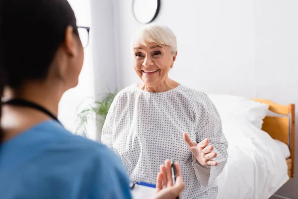 Mujer mayor feliz gesto mientras habla con la enfermera en el hospital, borrosa primer plano - foto de stock