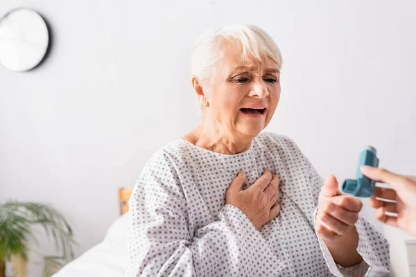 Alte Frau nimmt Inhalator von Krankenschwester, während sie unter Asthmaanfall leidet, verschwommener Vordergrund — Stockfoto