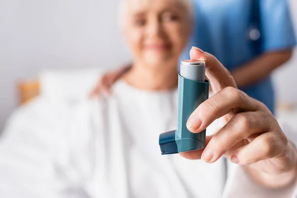 Alte Frau mit Inhalator nahe Krankenschwester im Krankenhaus, verschwommener Hintergrund — Stockfoto