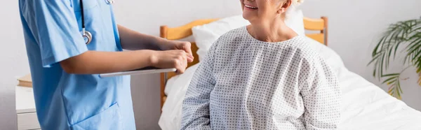 Vista recortada de la enfermera con tableta digital cerca de la mujer anciana sonriente en el hospital, pancarta - foto de stock