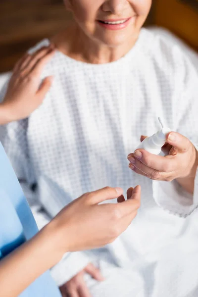 Cropped view of smiling senior woman holding nasal spray near nurse touching her shoulder, blurred background — Stock Photo