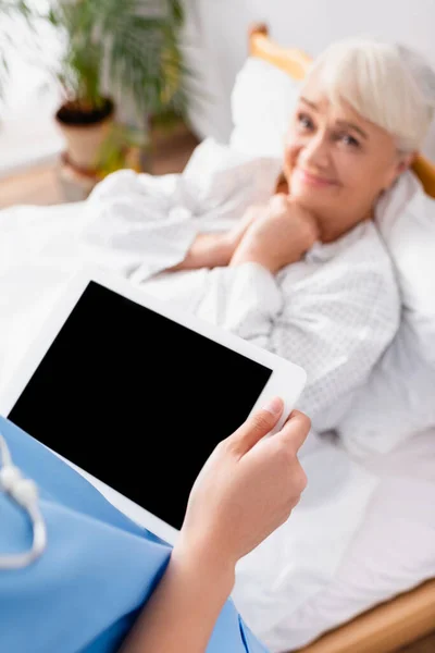 Feliz anciana mirando enfermera sosteniendo tableta digital con pantalla en blanco, fondo borroso - foto de stock