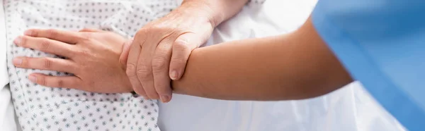Vista recortada de la mujer anciana tocando la mano de la enfermera en el hospital, bandera - foto de stock