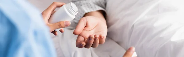 Vista recortada de la enfermera que sostiene el envase de medicamentos cerca del paciente anciano, pancarta - foto de stock