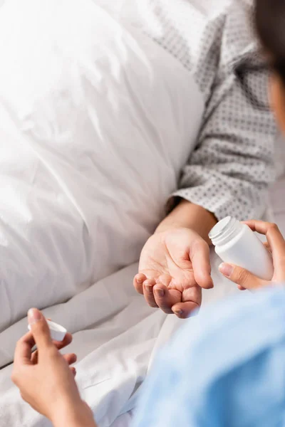 Partial view of nurse giving medicines to aged patient, blurred foreground — Stock Photo