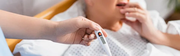 Teilaufnahme einer Krankenschwester mit Thermometer in der Nähe einer erkrankten Seniorin auf verschwommenem Hintergrund, Banner — Stockfoto