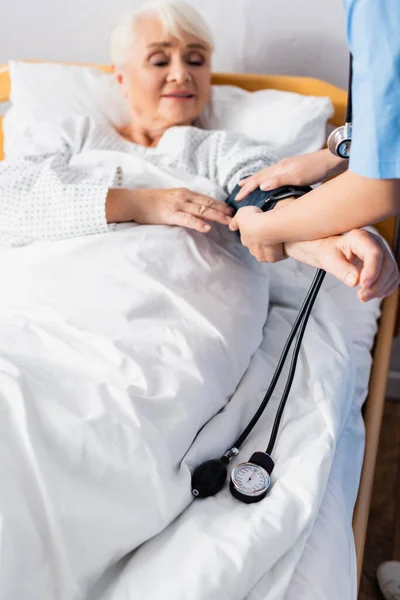 Infirmière mearing pression artérielle de la femme âgée avec tonomètre, fond flou — Photo de stock