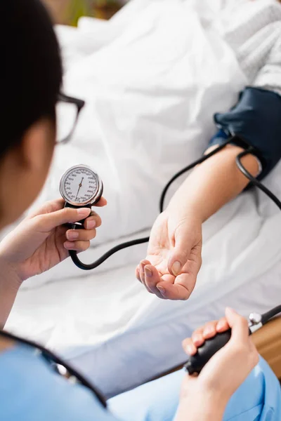 El foco selectivo de la presentación del tonómetro en las manos del enfermero que mide la presión arterial de la mujer anciana - foto de stock