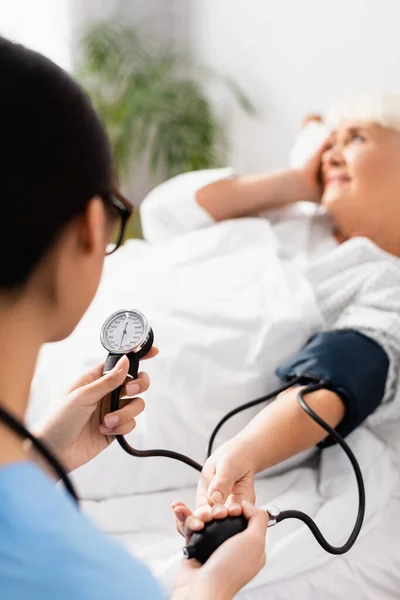 Mise au point sélective du tonomètre dans les mains de l'infirmière mesurant la pression artérielle de la femme âgée souffrant de maux de tête — Photo de stock