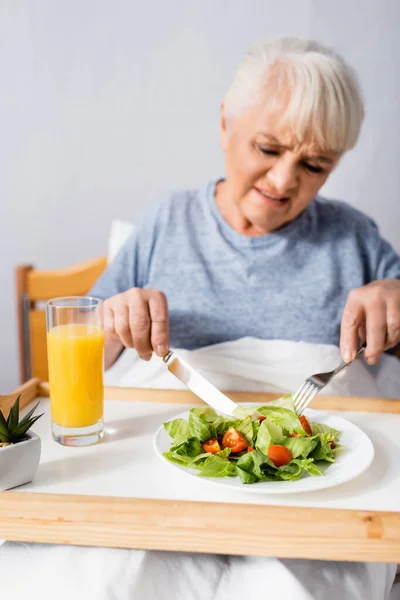 Displeased aged woman having breakfast in hospital, blurred foreground — Stock Photo