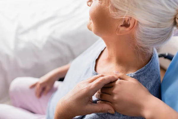 Обрезанный вид медсестры, трогающей плечо пожилой женщины в больнице, размытый фон — стоковое фото