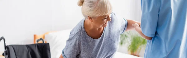 Nurse supporting elderly woman getting up from wheelchair, banner — Stock Photo