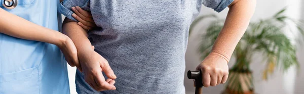 Teilaufnahme einer Krankenschwester, die eine alte Frau mit Gehstock unterstützt, Banner — Stockfoto