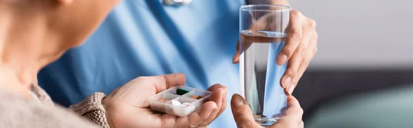 Partial view of nurse giving glass of water and pills to elderly patient, banner — Stock Photo