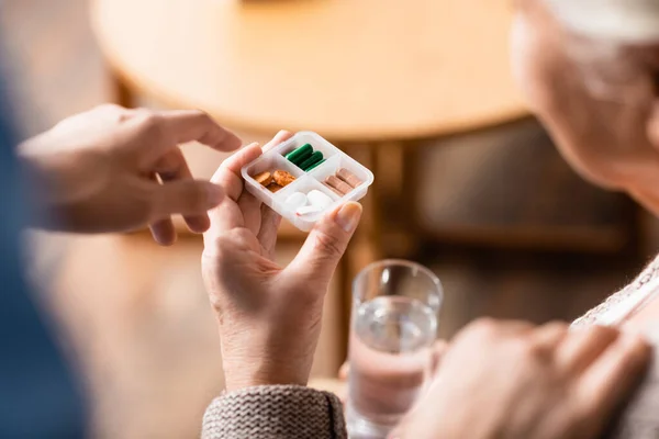 Ausgeschnittene Ansicht der Krankenschwester, die mit dem Finger auf Behälter mit Tabletten in der Hand eines älteren Patienten zeigt, selektiver Fokus — Stockfoto