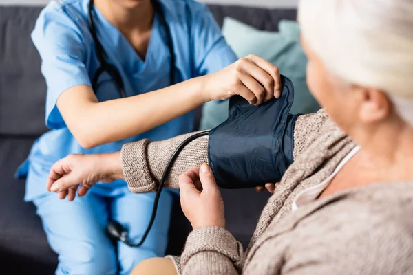 Cropped view of nurse fixing cuff of tonometer on arm of elderly woman — Stock Photo