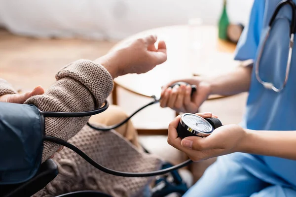 Teilaufnahme einer jungen Krankenschwester, die den Blutdruck einer Seniorin misst, verschwommener Hintergrund — Stockfoto