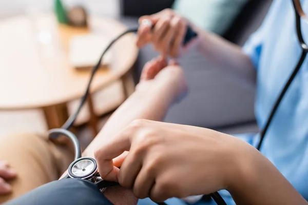 Vista recortada de la enfermera que mide la presión arterial del paciente con tonómetro, fondo borroso - foto de stock