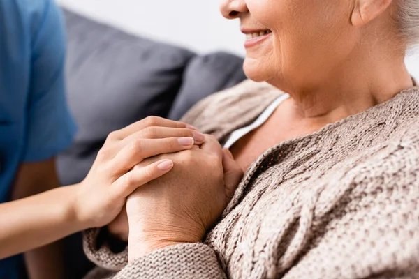 Ausgeschnittene Ansicht einer Krankenschwester, die Hände einer glücklichen älteren Frau im Pflegeheim berührt — Stockfoto