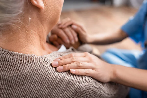 Обрезанный вид медсестры, трогательной руки и плеча пожилого пациента в доме престарелых, размытый фон — стоковое фото