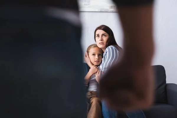 Scared woman hugging daughter near abusive husband on blurred foreground at home — Stock Photo