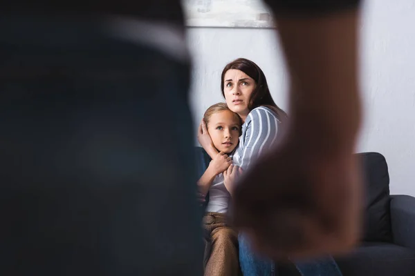 Verängstigte Frau umarmt Tochter neben missbräuchlichem Ehemann auf verschwommenem Vordergrund zu Hause — Stockfoto