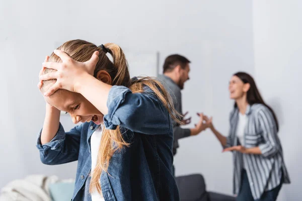 Screaming kid standing near parents quarrelling on blurred background — Stock Photo