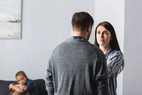 Scared woman standing near abuser and kid on couch on blurred background — Stock Photo