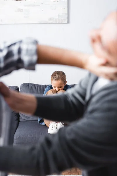 Niño molesto sentado en el sofá mientras los padres pelean en primer plano borroso - foto de stock