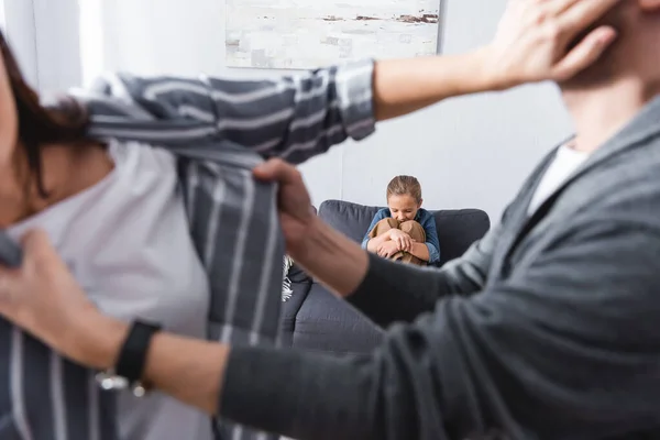 Deprimida chica sentada en el sofá mientras los padres pelean en primer plano borrosa - foto de stock