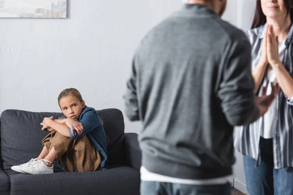 Chica asustada mirando a la madre de pie con las manos de oración cerca de padre abusivo en primer plano borrosa - foto de stock