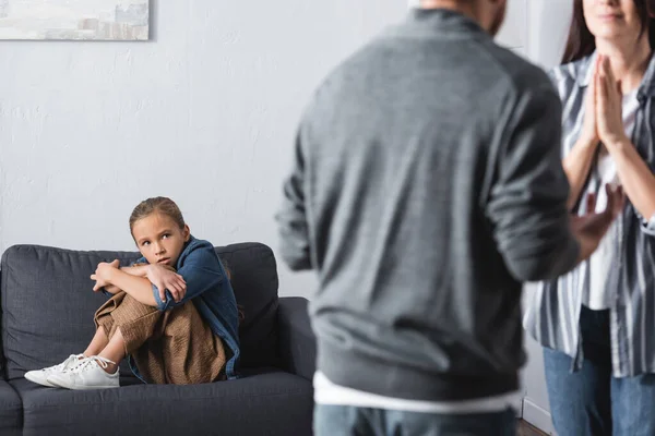 Fille effrayée regardant la mère debout avec les mains priantes près du père abusif sur le premier plan flou — Photo de stock