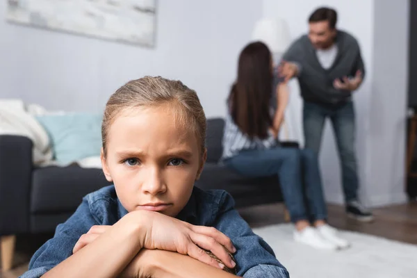 Trauriges Mädchen blickt in Kamera, während Eltern sich auf verschwommenem Hintergrund streiten — Stockfoto