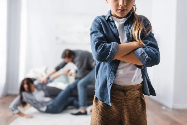 Girl with crossed arms standing near abusive father beating mother at home on blurred background — Stock Photo