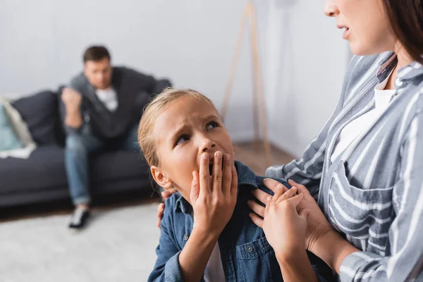 Frau umarmt verängstigtes Kind nahe missbräuchlichem Ehemann auf verschwommenem Hintergrund zu Hause — Stockfoto