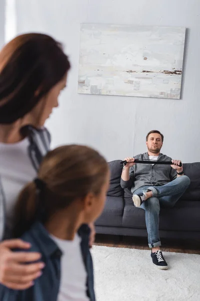 Hombre sosteniendo el cinturón de cintura mientras mira a su esposa e hijo en primer plano borroso - foto de stock