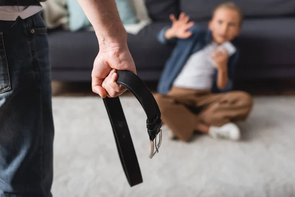 Homem segurando cinto de cintura perto de criança no chão em casa em fundo borrado — Fotografia de Stock