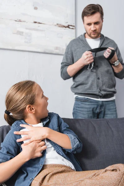 Scared child hiding smartphone and looking at father with waist belt on blurred background — Stock Photo