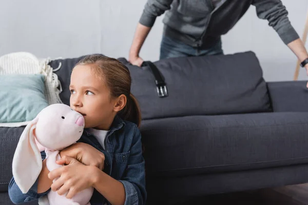 Girl holding soft toy near abusive father with waist belt on blurred background — Stock Photo