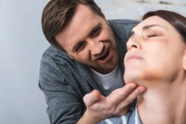 Disgusting husband looking at wife with bruises on face on blurred foreground at home — Stock Photo