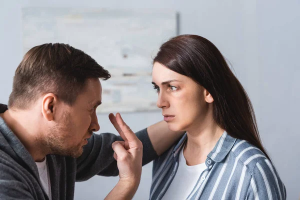 Abusive husband pointing at eyes near wife with bruise at home — Stock Photo