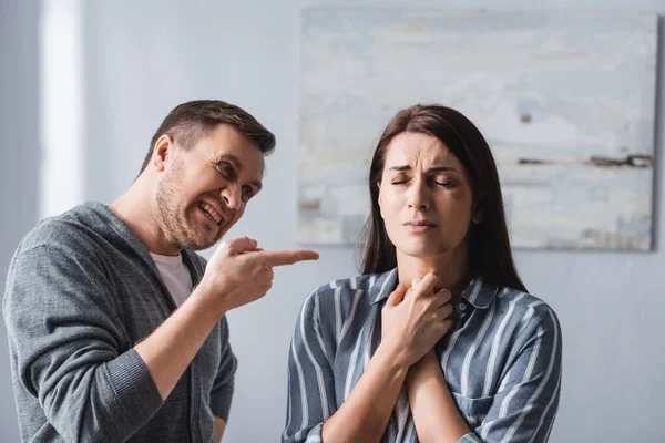 Wütender Mann zeigt mit Finger auf aufgebrachte Frau mit blauen Flecken zu Hause — Stockfoto