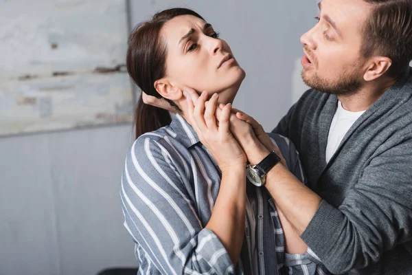 Abusive husband holding hair of scared wife with bruise on hand at home — Stock Photo