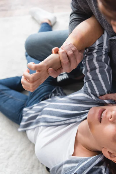 Vista de ángulo alto del abusador comprimiendo la mano de la esposa con moretones en casa - foto de stock