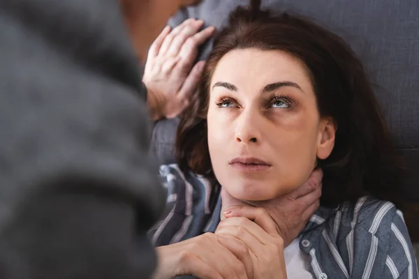 Donna soffocante con lividi sul viso vicino al marito abusivo in primo piano sfocato — Foto stock