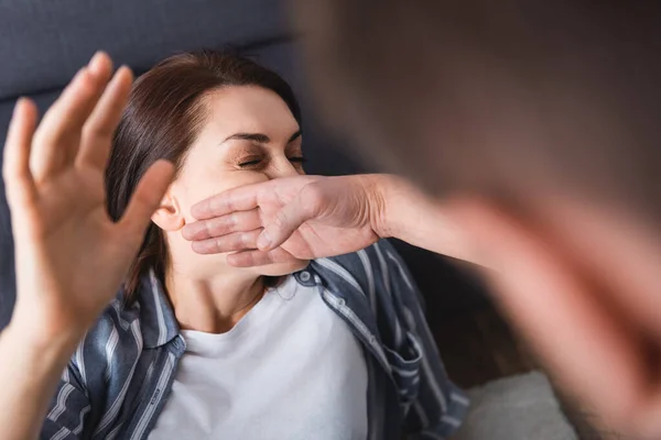 Abuser slapping wife near couch on blurred background at home — Stock Photo