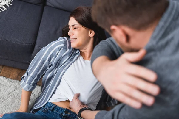 Abuser on blurred foreground beating scared wife with bruises on face near couch — Stock Photo