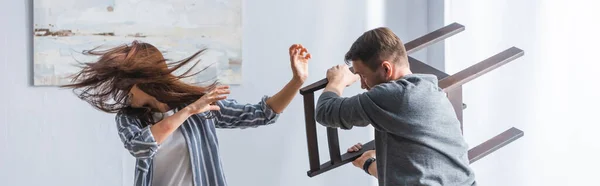 Victim of domestic violence screaming near husband with chair at home, banner — Stock Photo