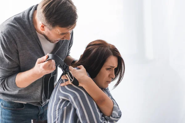Grito abusador segurando cinto perto da esposa com hematomas em casa — Fotografia de Stock